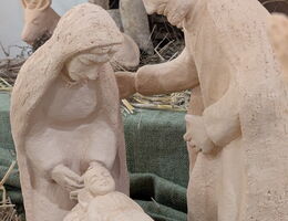 Handgefertigte Krippenfiguren von Maria, Josef und Jesuskind, umgeben von Stroh.