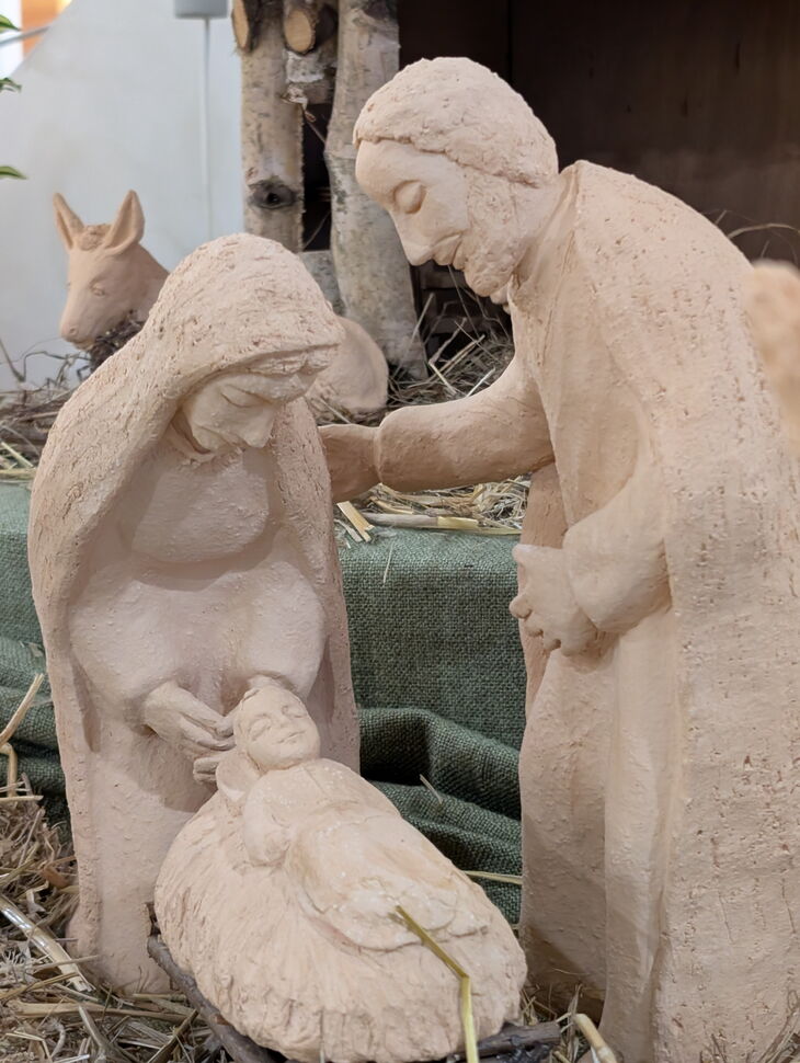 Handgefertigte Krippenfiguren von Maria, Josef und Jesuskind, umgeben von Stroh.