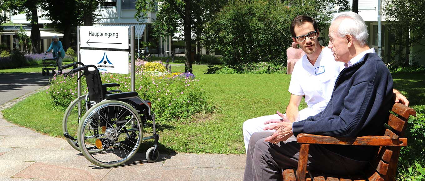 Ein Pfleger und ein alter Herr auf einer Bank vor dem Altenzentrum