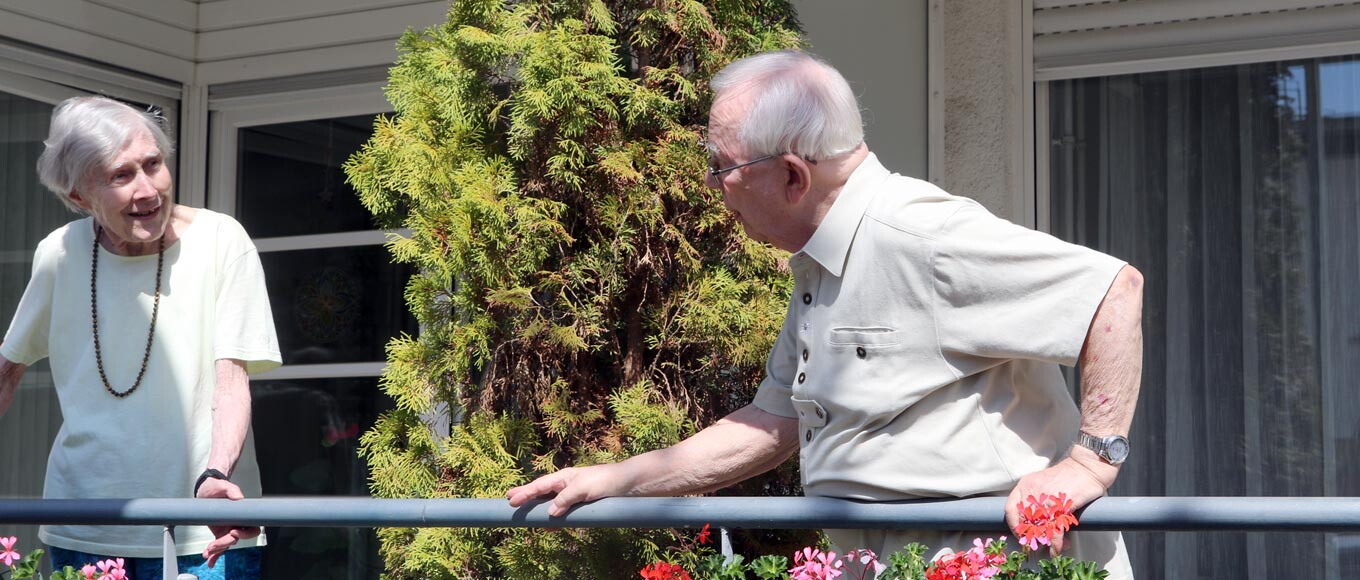 Eine alte Frau und ein alter Mann unterhalten sich auf dem Balkon